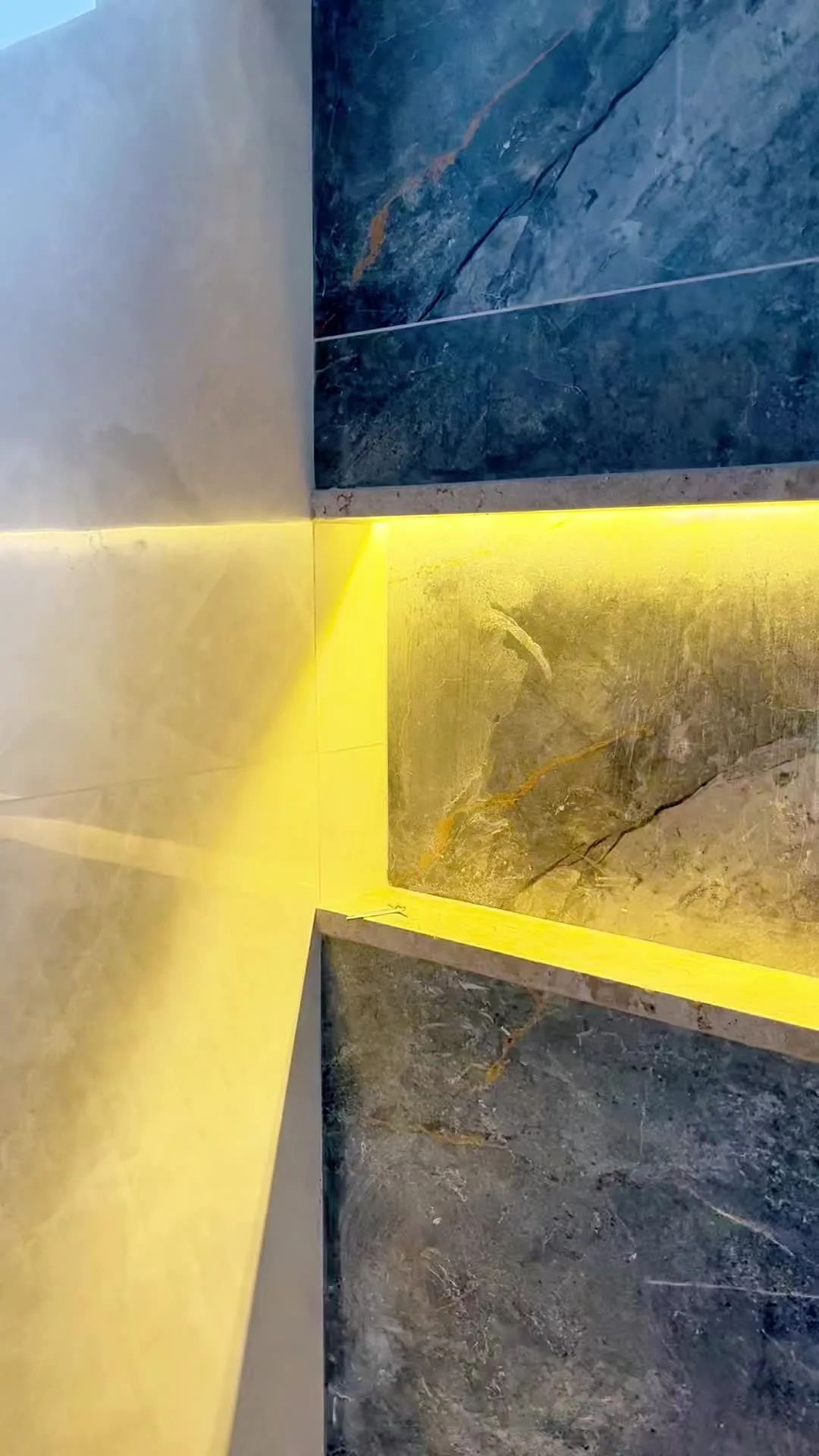 Detalhe de parede em pedra escura com iluminação embutida.