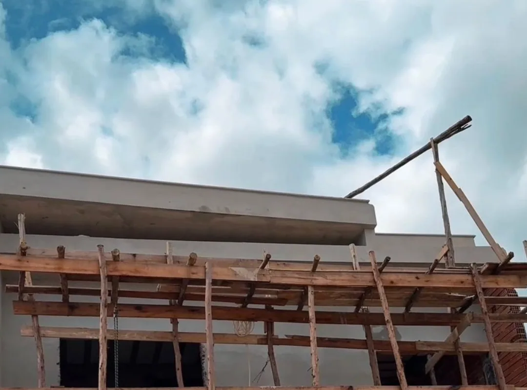 Casa em construção com andaimes de madeira sob céu com nuvens.