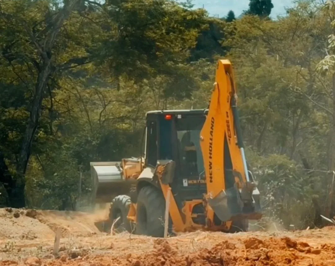 Retroescavadeira preparando um terreno cercado de árvores.