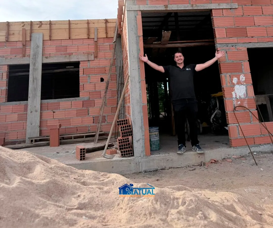 Homem de camisa da Atual de braços abertos na porta de uma casa em construção.